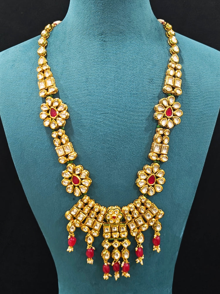 Close-up of an ornate traditional (Gold Polish) White Long jewellery set and earrings with Kundan, Red Colored Stone and Red Beads. Woman wearing trending Kundan artificial jewelry for wedding season in India. Wedding guest wearing a lightweight Kundan necklace for a festive function.