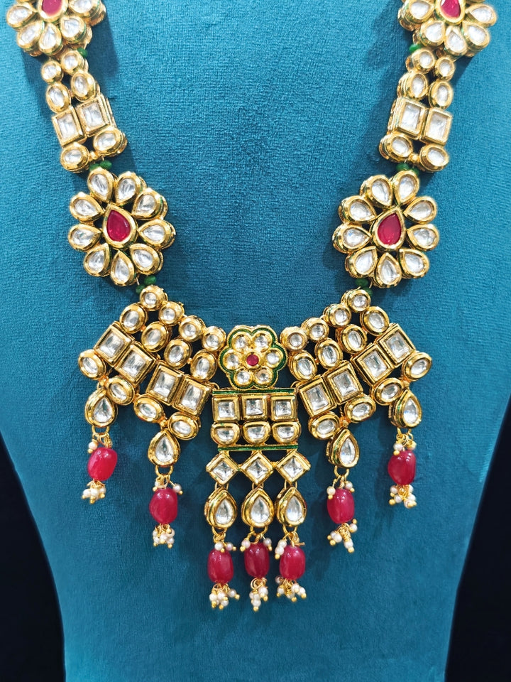 Close-up of an ornate traditional (Gold Polish) White Long jewellery set and earrings with Kundan, Red Colored Stone and Red Beads. Woman wearing trending Kundan artificial jewelry for wedding season in India. Wedding guest wearing a lightweight Kundan necklace for a festive function.