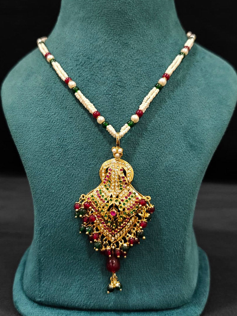 Close-up of an ornate traditional Maroon and Dark Green jadau gold Pendant set and jadau earrings with pearls, Beads and Color Stone. Elegant  look featuring a luxury Jadau artificial Pendant set. Festive celebration look featuring a Jadau artificial Pendant Set.