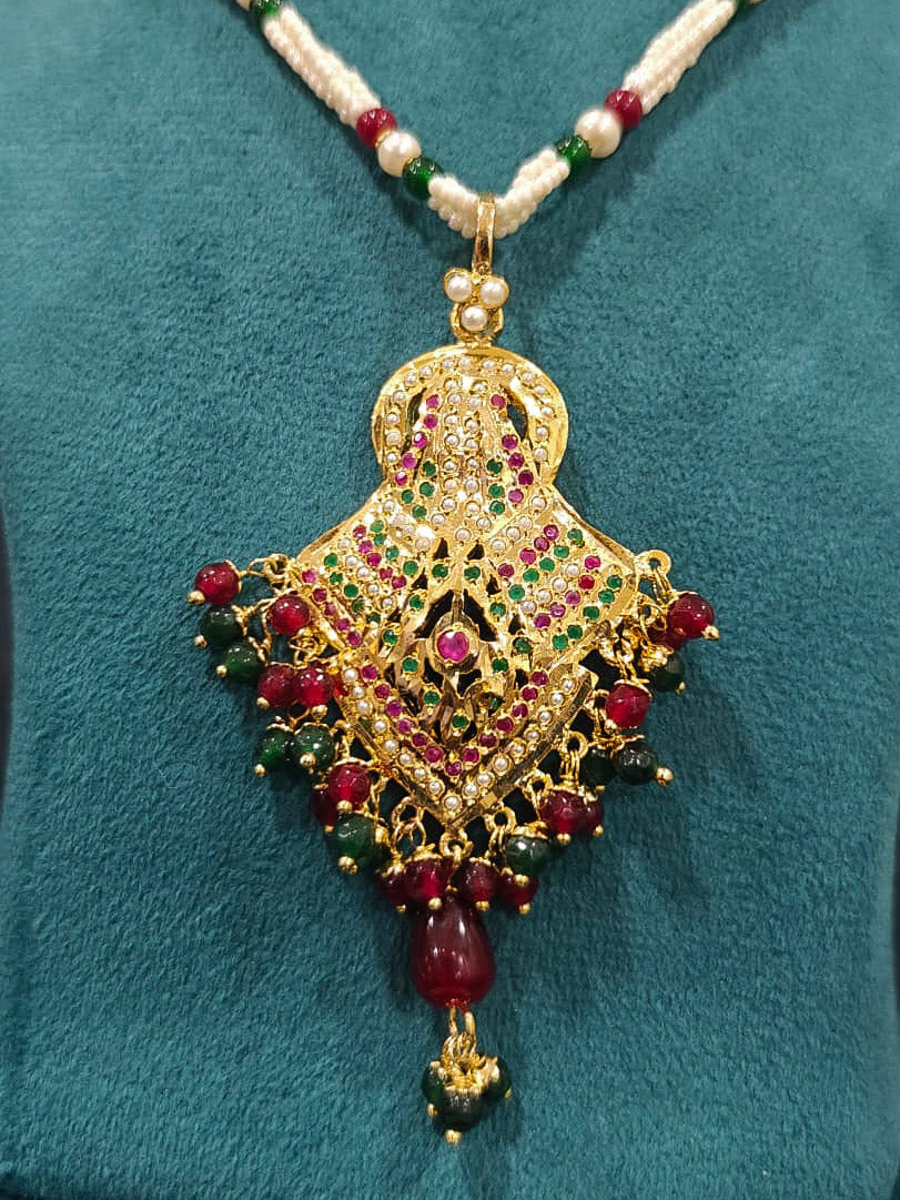 Close-up of an ornate traditional Maroon and Dark Green jadau gold Pendant set and jadau earrings with pearls, Beads and Color Stone. Elegant  look featuring a luxury Jadau artificial Pendant set. Festive celebration look featuring a Jadau artificial Pendant Set.