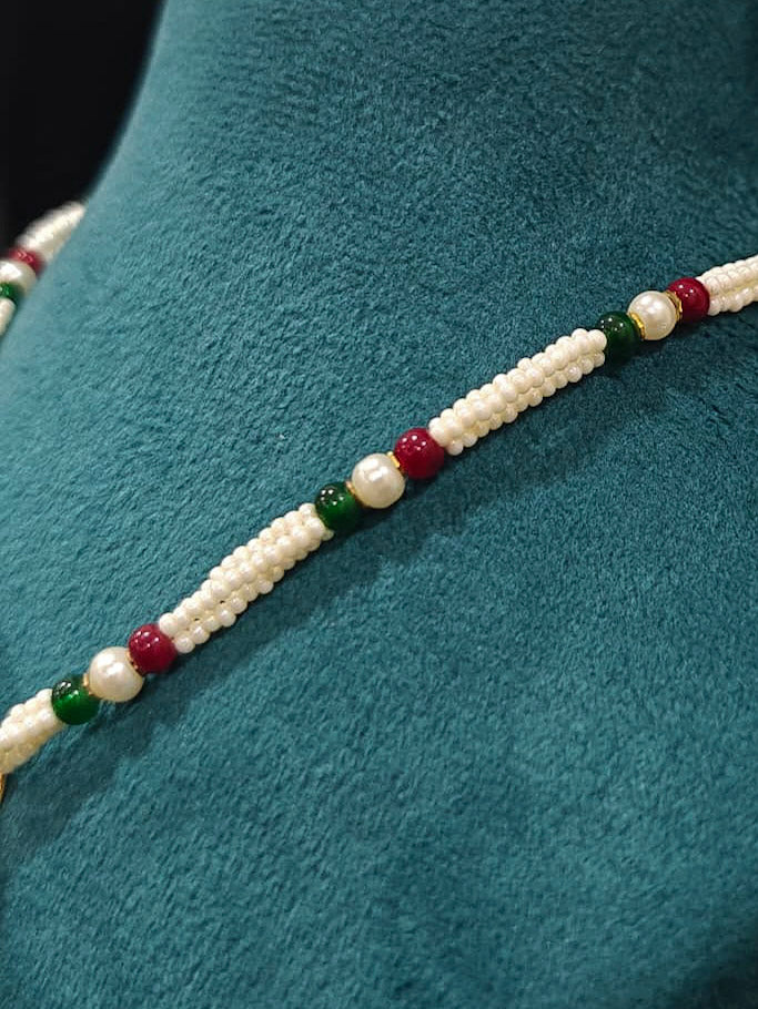 Close-up of an ornate traditional Maroon and Dark Green jadau gold Pendant set and jadau earrings with pearls, Beads and Color Stone. Elegant  look featuring a luxury Jadau artificial Pendant set. Festive celebration look featuring a Jadau artificial Pendant Set.