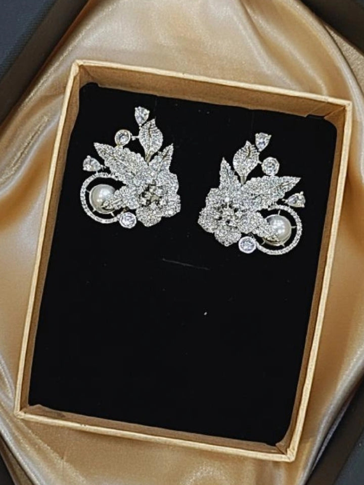 Zephyra Earrings: Ornate white earrings featuring floral and leaf designs, embellished with American diamonds and pearls, presented in a black velvet box on gold satin—ideal for accessorizing your wedding ceremony dress.