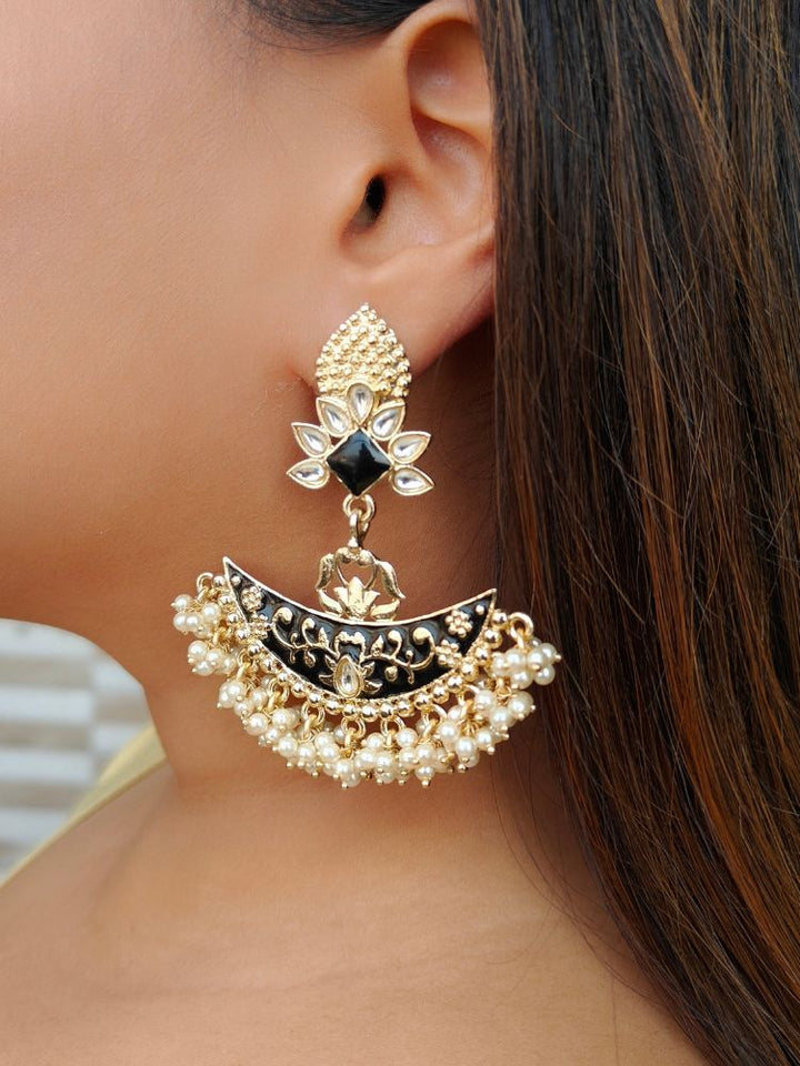 A close-up of a womans ear wearing the Zoha Black Earrings—large Chandbali-style with black enamel, gold detailing, pearl beads, floral motifs, and intricate Kundan Meenakari work in a crescent shape with a floral stud.