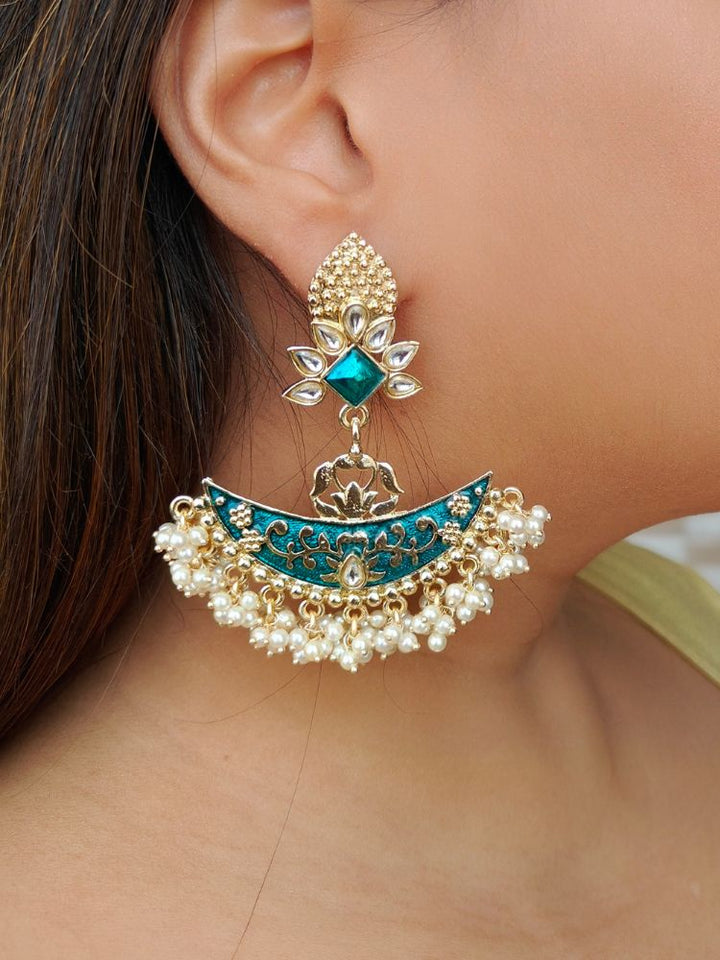 A close-up of a womans ear wearing the Zoha Blue Earrings—large Chandbali-style with blue enamel, gold detailing, pearl beads, floral motifs, and intricate Kundan Meenakari work in a crescent shape with a floral stud.