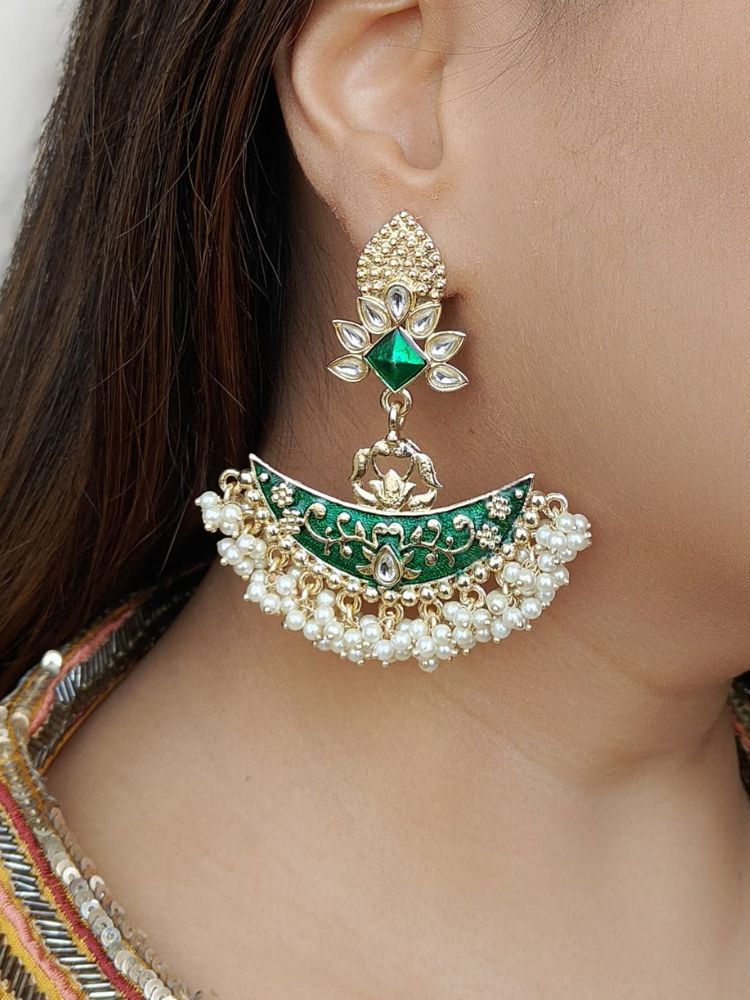 A close-up of a womans ear wearing the Zoha Green Earrings—large Chandbali-style with Green enamel, gold detailing, pearl beads, floral motifs, and intricate Kundan Meenakari work in a crescent shape with a floral stud.