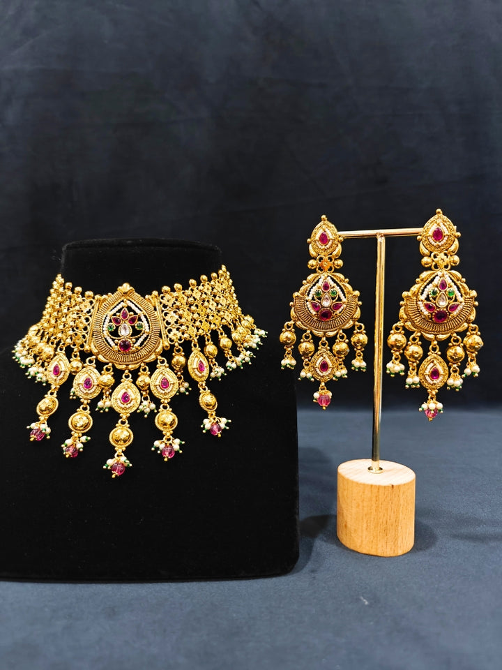 Close-up of an ornate traditional (Bright Gold Polish) Choker jewellery set and earrings with Pearl and Colored Stone. Woman wearing a vibrant Colored Stone artificial jewelry set for celebrations. Wedding function styling with a premium Colored Stone imitation necklace.