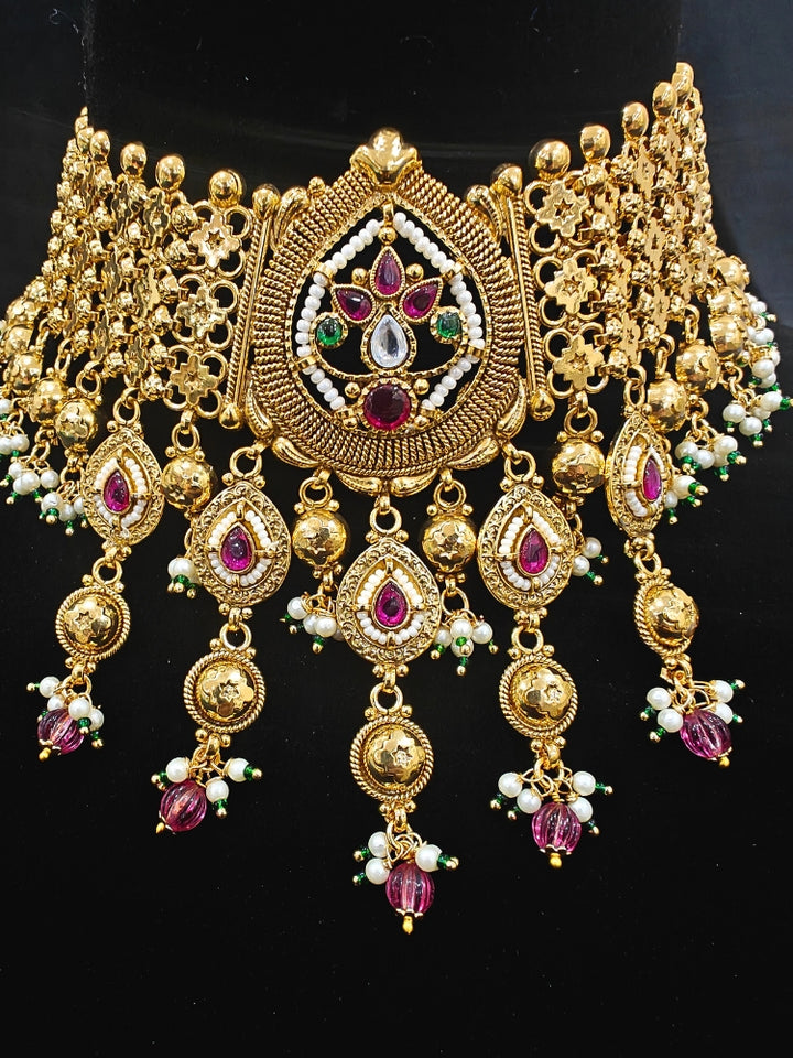 Close-up of an ornate traditional (Bright Gold Polish) Choker jewellery set and earrings with Pearl and Colored Stone. Woman wearing a vibrant Colored Stone artificial jewelry set for celebrations. Wedding function styling with a premium Colored Stone imitation necklace.