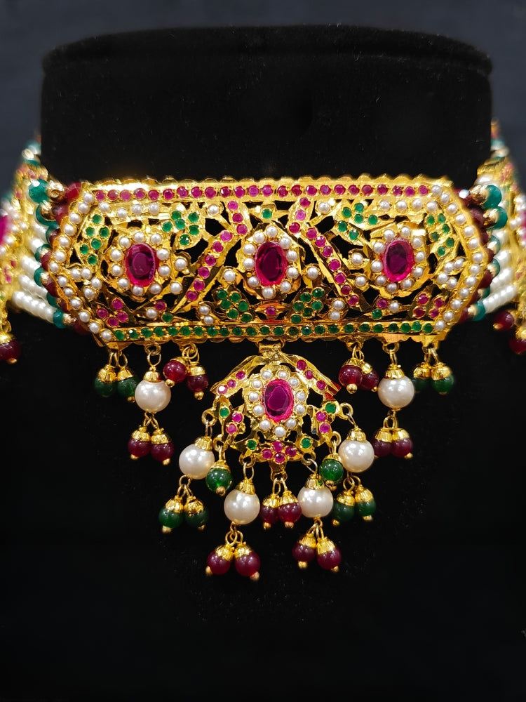 Close-up of a woman wearing an ornate traditional Choker jadau gold jewellery set and  jadau earrings with crystals beads and gemstones. Perfect Jadau necklace set for weddings and festivals. Elegant reception look featuring a luxury Jadau artificial jewelry set.