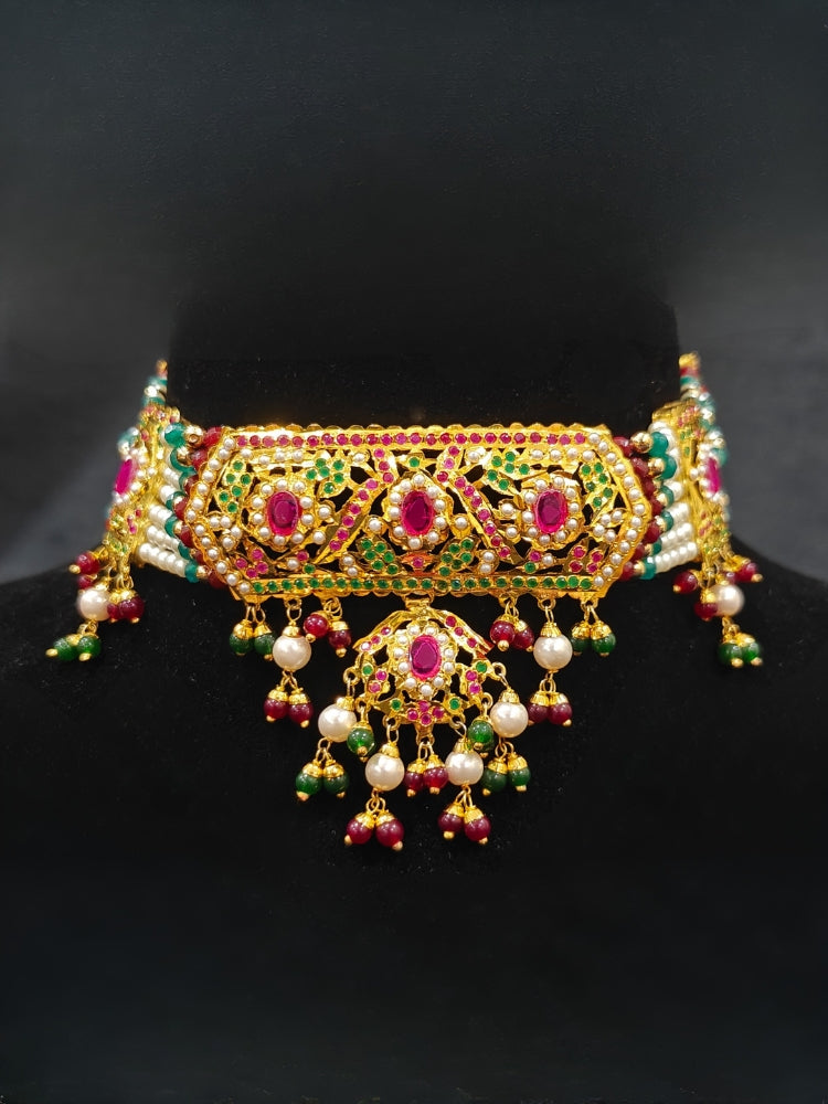 Close-up of a woman wearing an ornate traditional Choker jadau gold jewellery set and  jadau earrings with crystals beads and gemstones. Perfect Jadau necklace set for weddings and festivals. Elegant reception look featuring a luxury Jadau artificial jewelry set.