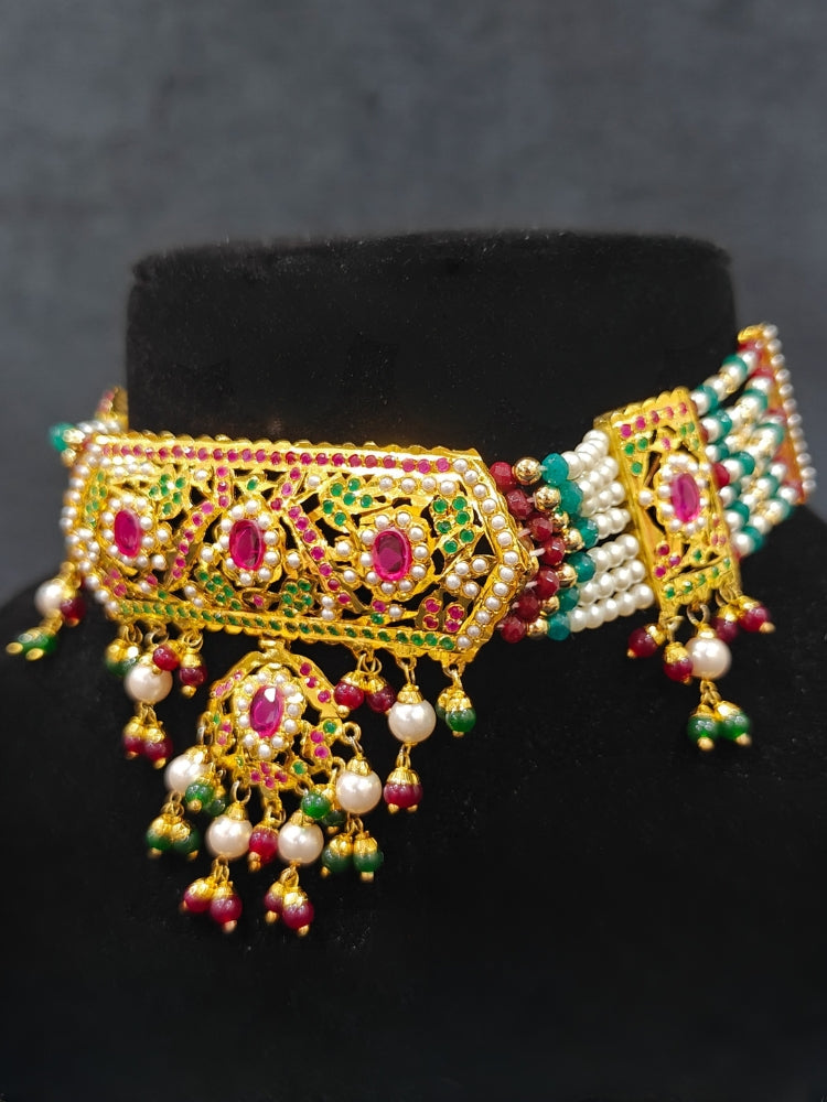 Close-up of a woman wearing an ornate traditional Choker jadau gold jewellery set and  jadau earrings with crystals beads and gemstones. Perfect Jadau necklace set for weddings and festivals. Elegant reception look featuring a luxury Jadau artificial jewelry set.