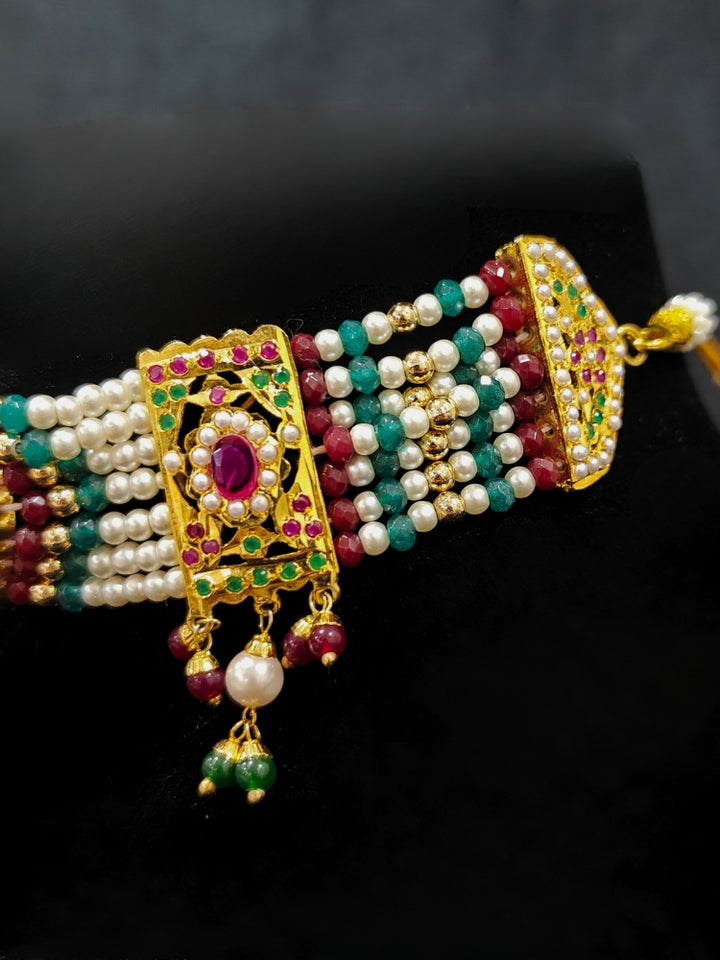 Close-up of a woman wearing an ornate traditional Choker jadau gold jewellery set and  jadau earrings with crystals beads and gemstones. Perfect Jadau necklace set for weddings and festivals. Festive celebration look featuring a Jadau artificial necklace.
