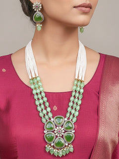 Close-up of a woman wearing an ornate traditional (Black Polish) Mehendi Green long jewellery set and earrings with Mehendi Green Colored Stones, Tumble Beads, Pearls and American Diamond. Woman wearing trending Colored Stone artificial jewelry for wedding season in India. Festive celebration look enhanced with traditional Colored Stone jewelry.