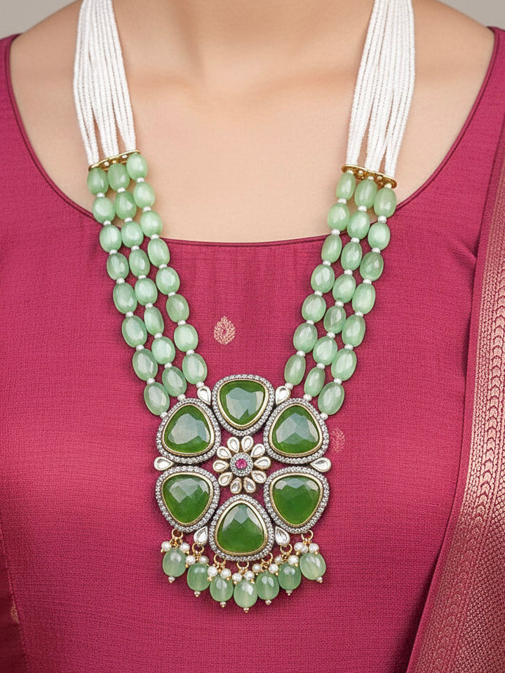 Close-up of a woman wearing an ornate traditional (Black Polish) Mehendi Green long jewellery set and earrings with Mehendi Green Colored Stones, Tumble Beads, Pearls and American Diamond. Woman wearing trending Colored Stone artificial jewelry for wedding season in India. Festive celebration look enhanced with traditional Colored Stone jewelry.