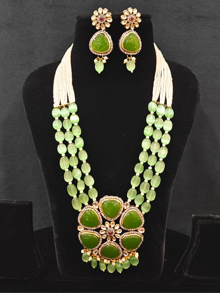 Close-up of an ornate traditional (Black Polish) Mehendi Green long jewellery set and earrings with Mehendi Green Colored Stones, Tumble Beads, Pearls and American Diamond. Woman wearing trending Colored Stone artificial jewelry for wedding season in India. Festive celebration look enhanced with traditional Colored Stone jewelry.