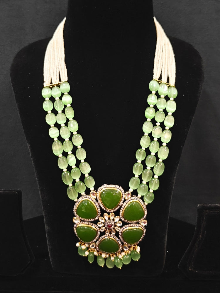 Close-up of an ornate traditional (Black Polish) Mehendi Green long jewellery set and earrings with Mehendi Green Colored Stones, Tumble Beads, Pearls and American Diamond. Woman wearing trending Colored Stone artificial jewelry for wedding season in India. Festive celebration look enhanced with traditional Colored Stone jewelry.