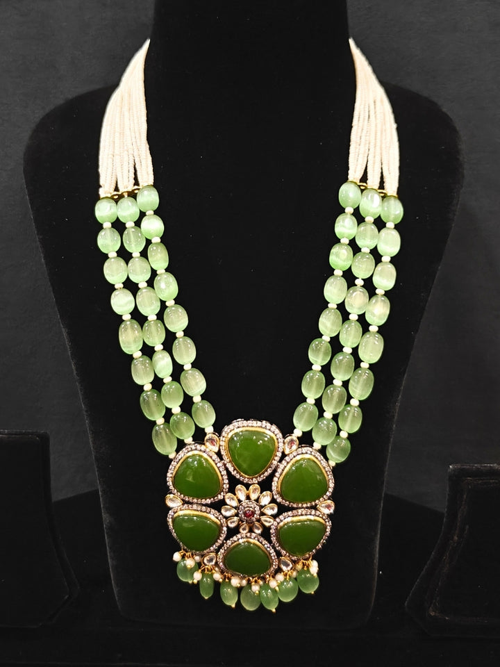 Close-up of an ornate traditional (Black Polish) Mehendi Green long jewellery set and earrings with Mehendi Green Colored Stones, Tumble Beads, Pearls and American Diamond. Woman wearing trending Colored Stone artificial jewelry for wedding season in India. Festive celebration look enhanced with traditional Colored Stone jewelry.
