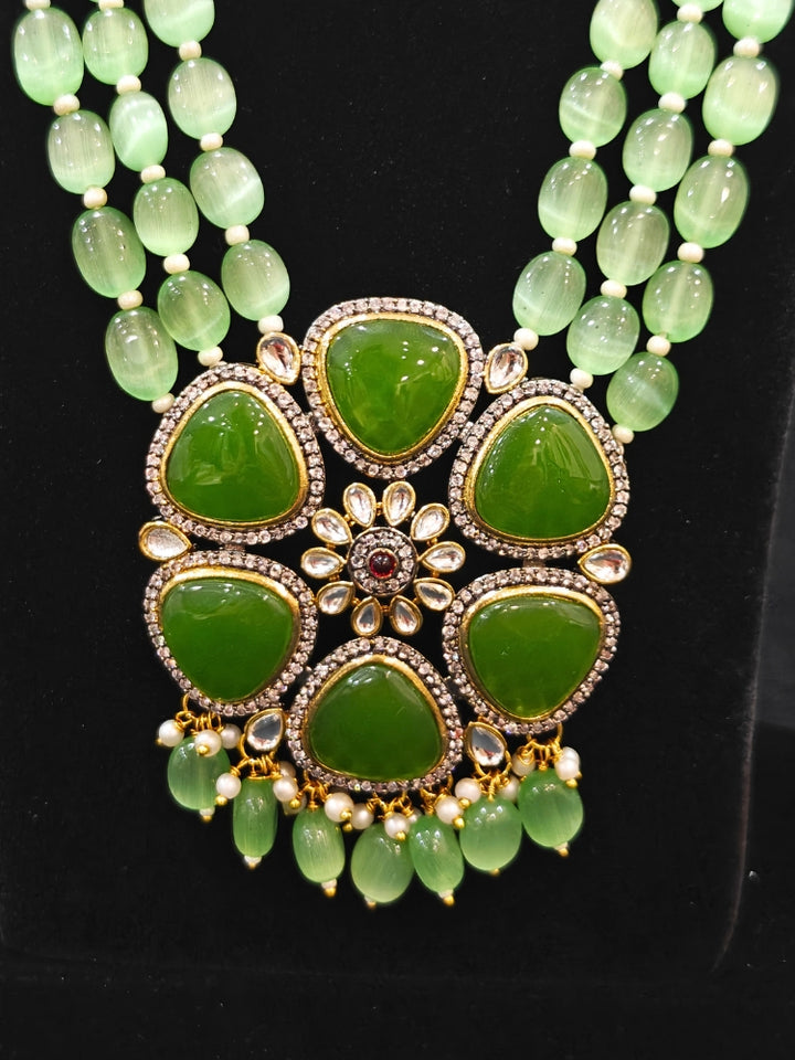 Close-up of an ornate traditional (Black Polish) Mehendi Green long jewellery set and earrings with Mehendi Green Colored Stones, Tumble Beads, Pearls and American Diamond. Woman wearing trending Colored Stone artificial jewelry for wedding season in India. Festive celebration look enhanced with traditional Colored Stone jewelry.
