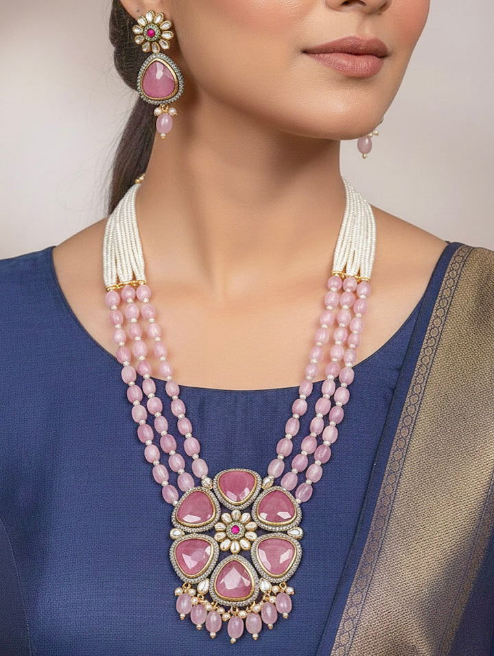 Close-up of a woman wearing an ornate traditional Pink long jewellery set and earrings with Pink Colored Stones, Tumble Beads, Pearls and American Diamond. Woman wearing trending Colored Stone artificial jewelry for wedding season in India. Festive celebration look enhanced with traditional Colored Stone jewelry.
