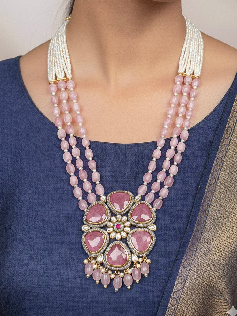Close-up of a woman wearing an ornate traditional Pink long jewellery set and earrings with Pink Colored Stones, Tumble Beads, Pearls and American Diamond. Woman wearing trending Colored Stone artificial jewelry for wedding season in India. Festive celebration look enhanced with traditional Colored Stone jewelry.