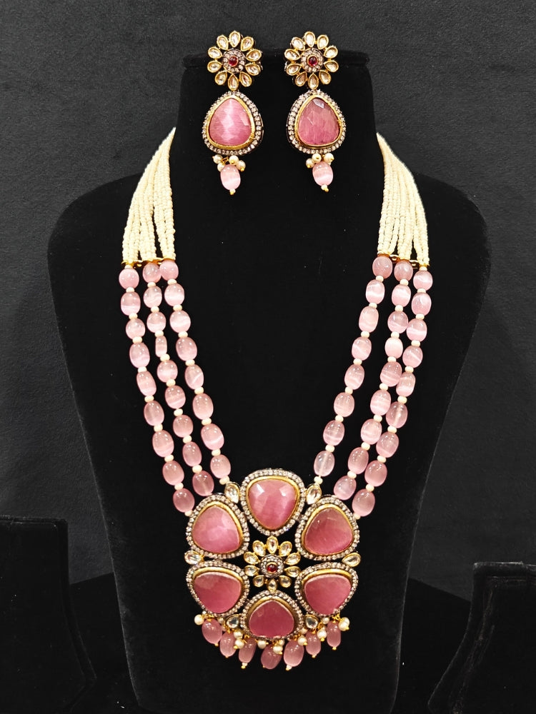 Close-up of an ornate traditional Pink long jewellery set and earrings with Pink Colored Stones, Tumble Beads, Pearls and American Diamond. Woman wearing trending Colored Stone artificial jewelry for wedding season in India. Festive celebration look enhanced with traditional Colored Stone jewelry.