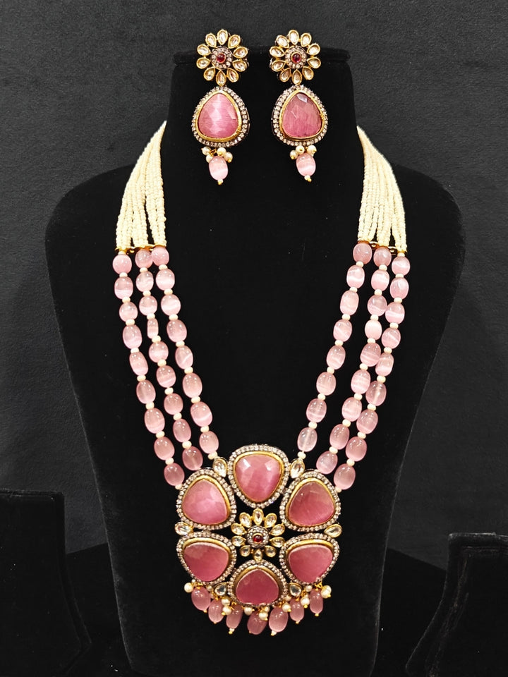 Close-up of an ornate traditional Pink long jewellery set and earrings with Pink Colored Stones, Tumble Beads, Pearls and American Diamond. Woman wearing trending Colored Stone artificial jewelry for wedding season in India. Festive celebration look enhanced with traditional Colored Stone jewelry.