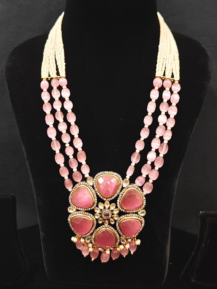 Close-up of an ornate traditional Pink long jewellery set and earrings with Pink Colored Stones, Tumble Beads, Pearls and American Diamond. Woman wearing trending Colored Stone artificial jewelry for wedding season in India. Festive celebration look enhanced with traditional Colored Stone jewelry.