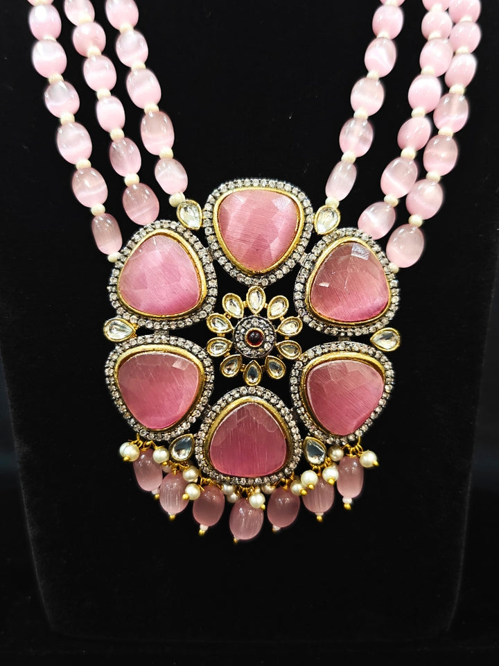 Close-up of an ornate traditional Pink long jewellery set and earrings with Pink Colored Stones, Tumble Beads, Pearls and American Diamond. Woman wearing trending Colored Stone artificial jewelry for wedding season in India. Festive celebration look enhanced with traditional Colored Stone jewelry.