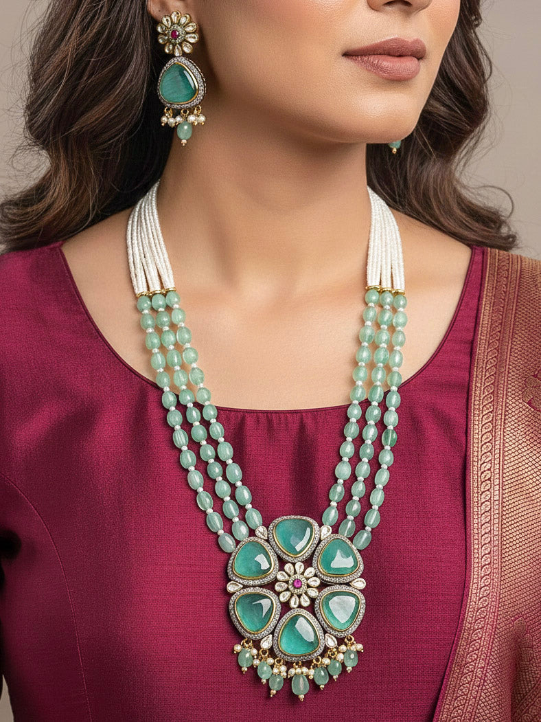Close-up of a woman wearing an ornate traditional (Black Polish) Sea Green long jewellery set and earrings with Sea Green Colored Stones, Tumble Beads, Pearls and American Diamond. Woman wearing trending Colored Stone artificial jewelry for wedding season in India. Festive celebration look enhanced with traditional Colored Stone jewelry.