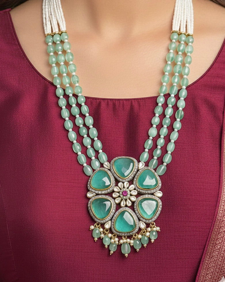 Close-up of a woman wearing an ornate traditional (Black Polish) Sea Green long jewellery set and earrings with Sea Green Colored Stones, Tumble Beads, Pearls and American Diamond. Woman wearing trending Colored Stone artificial jewelry for wedding season in India. Festive celebration look enhanced with traditional Colored Stone jewelry.