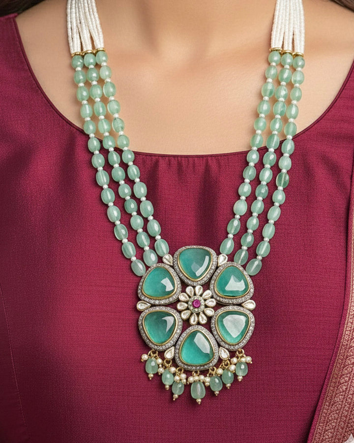 Close-up of a woman wearing an ornate traditional (Black Polish) Sea Green long jewellery set and earrings with Sea Green Colored Stones, Tumble Beads, Pearls and American Diamond. Woman wearing trending Colored Stone artificial jewelry for wedding season in India. Festive celebration look enhanced with traditional Colored Stone jewelry.
