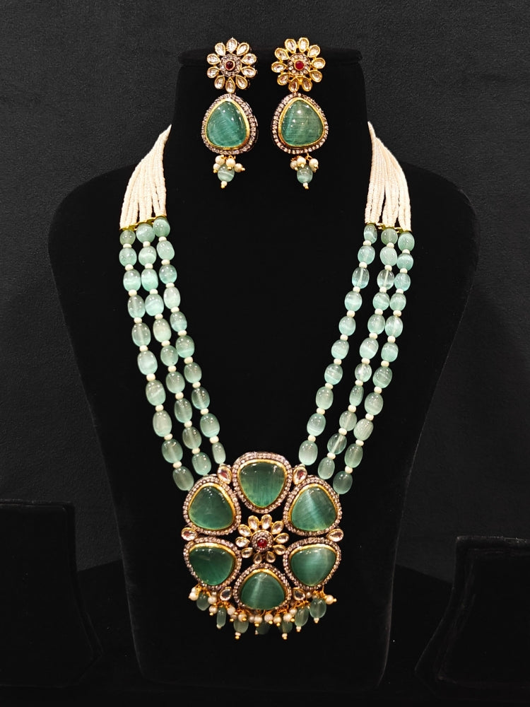 Close-up of an ornate traditional (Black Polish) Sea Green long jewellery set and earrings with Sea Green Colored Stones, Tumble Beads, Pearls and American Diamond. Woman wearing trending Colored Stone artificial jewelry for wedding season in India. Festive celebration look enhanced with traditional Colored Stone jewelry.
