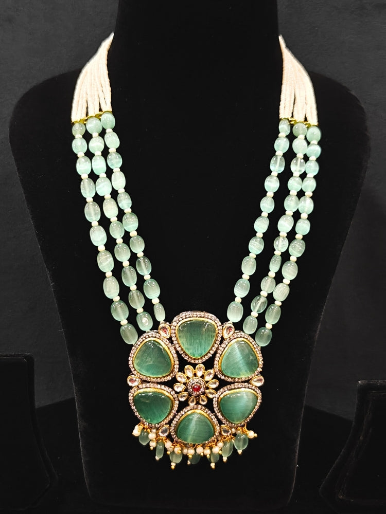 Close-up of an ornate traditional (Black Polish) Sea Green long jewellery set and earrings with Sea Green Colored Stones, Tumble Beads, Pearls and American Diamond. Woman wearing trending Colored Stone artificial jewelry for wedding season in India. Festive celebration look enhanced with traditional Colored Stone jewelry.