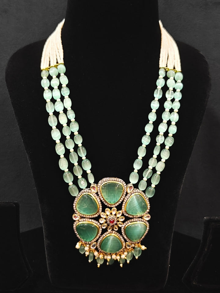 Close-up of an ornate traditional (Black Polish) Sea Green long jewellery set and earrings with Sea Green Colored Stones, Tumble Beads, Pearls and American Diamond. Woman wearing trending Colored Stone artificial jewelry for wedding season in India. Festive celebration look enhanced with traditional Colored Stone jewelry.