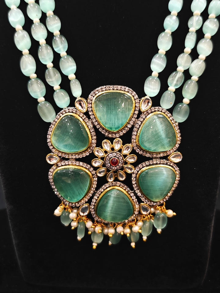 Close-up of an ornate traditional (Black Polish) Sea Green long jewellery set and earrings with Sea Green Colored Stones, Tumble Beads, Pearls and American Diamond. Woman wearing trending Colored Stone artificial jewelry for wedding season in India. Festive celebration look enhanced with traditional Colored Stone jewelry.